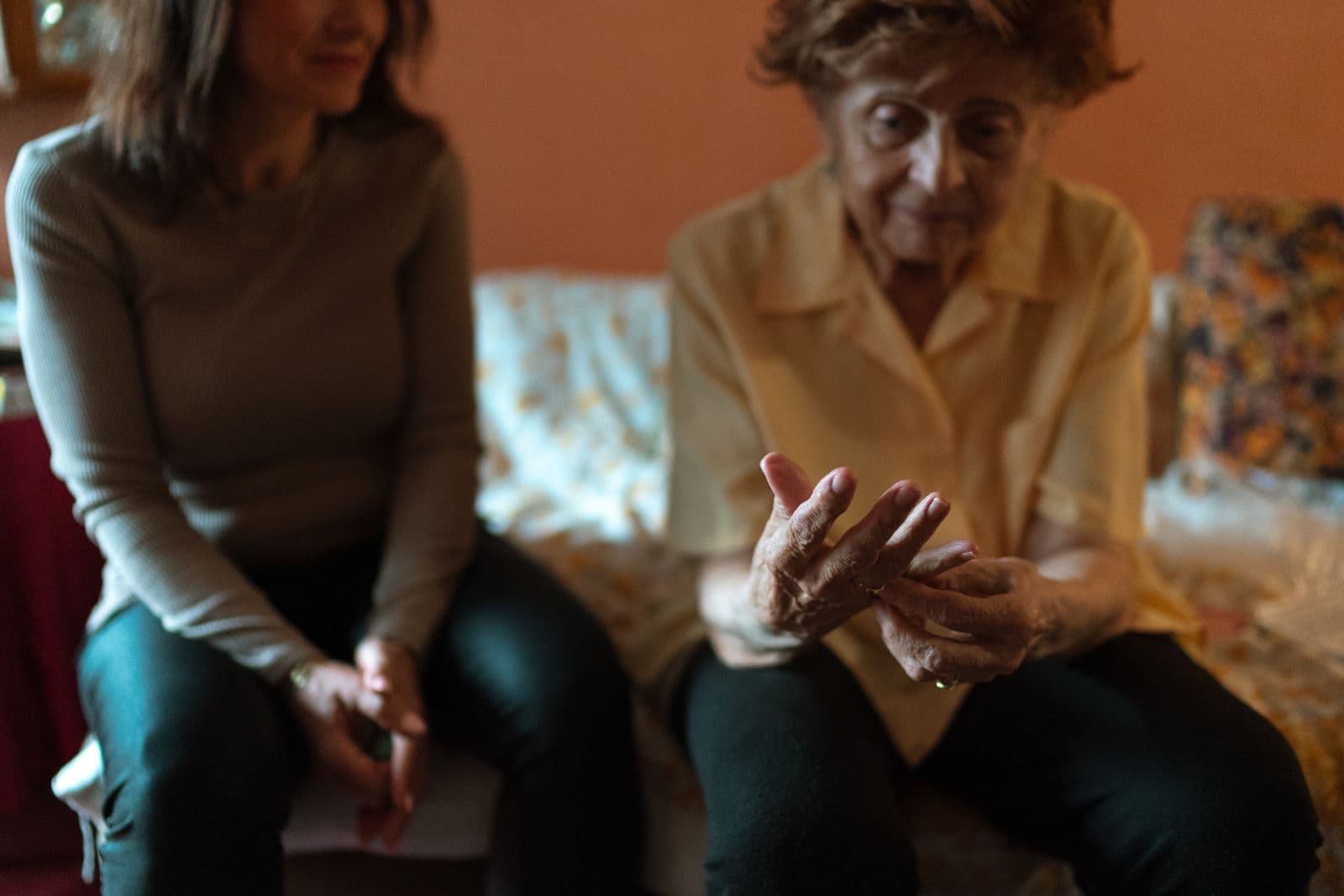 A caregiver sits beside a resident, holding her hand